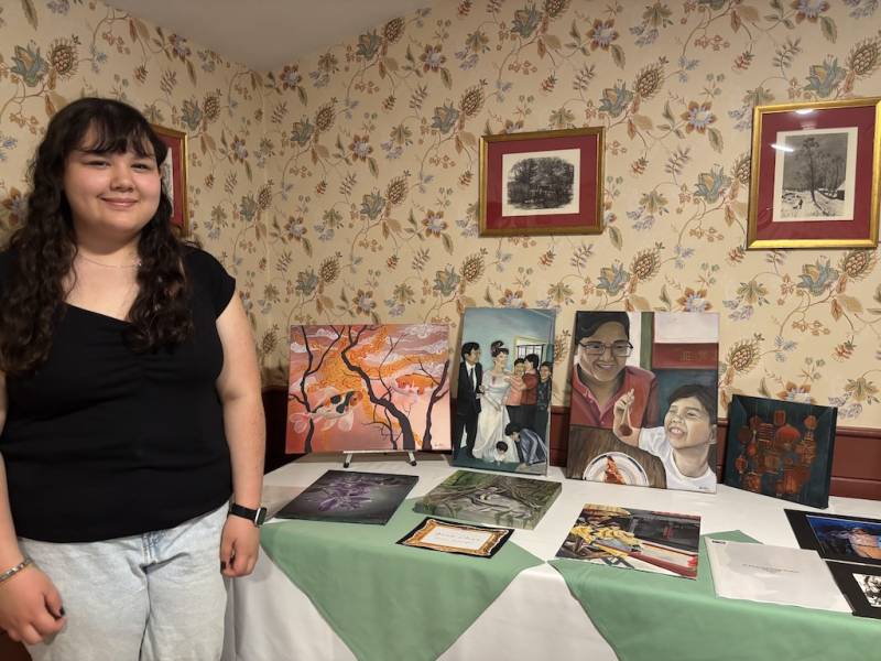 Anna Chenstands beside her art at the show, featuring portraits and other designs.